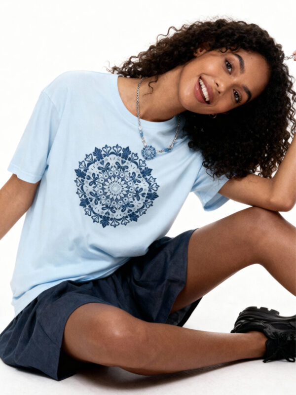 A brunette woman wearing a light blue 'Gildan 64000' t-shirt with a detailed navy blue oriental mandala graphic, styled for a minimalist zen look.